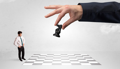 Little businessman thinking about chess strategy with a big hand concept
