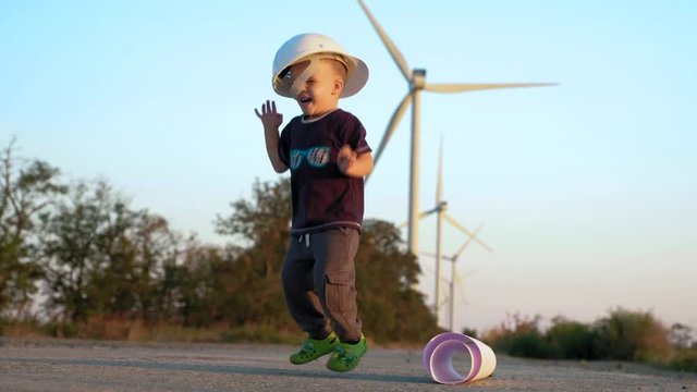 A little boy plays with constructor helmet. He puts it on and jumps until it falls down