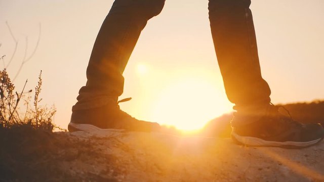 Hiker walking outdoors at sunset on the rock. Legs in trekking boots go along the mountain ridge against the backdrop of the sun Close up of leg walking in slow motion. Travel and adventure concept.