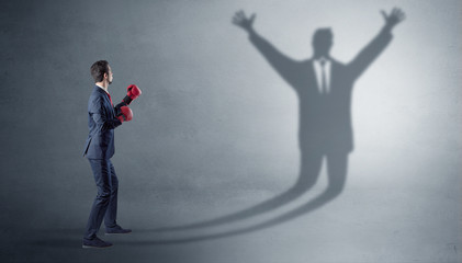 Businessman with boxing gloves fighting with disarmed businessman shadow
