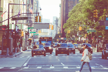 New York City street road in Manhattan at summer time, many cars, yellow taxis and busy people walk...