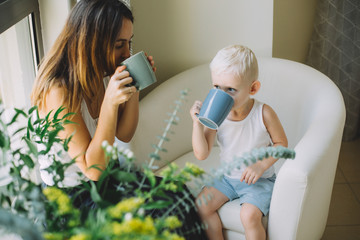 Mother and her little son holding cups sitting on a sofa