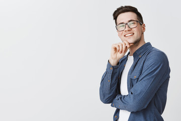 Delighted happy and satisfied handsome young male student in glasses and blue shirt holding hand on...