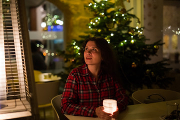 Holiday, Christmas and people concept - Young woman sitting in cafe near Christmas tree background at night