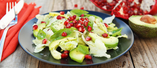 Vegetarian salad with avocado, greens, leaves, pomegranate and letuce leaves. Wooden rustic table.