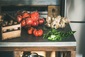 Modern kitchen concrete counter with ingredients for cooking tomato sauce, canned tomatoes or pasta dish with heirloom tomatoes, garlic and basil. Healthy seasonal cooking, slow food