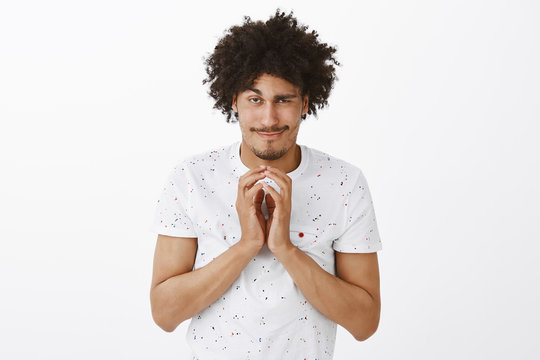Evil genius have great plan to conquer world. Tricky and mysterious funny hispanic guy with curly hair, steeping fingers and smirking at camera, lifting one eyebrow, having bad intention in mind