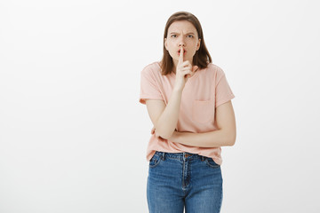 Shut your mouth, keep silent. Portrait of pissed angry woman in pink t-shirt and jeans, saying shh while making shush gesture with index finger over mouth, frowning, asking friend to be quiet