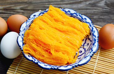 Golden egg strip is Thai desserts made from eggs with Thai style bowl on wooden background ( Thai name is Foi Thong). © posinote