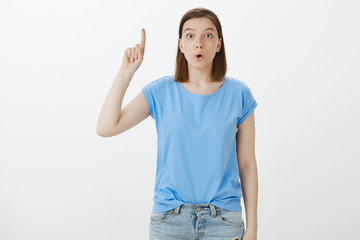 I have great idea, listen. Portrait of excited attractive caucasian girlfriend in blue t-short raising index finger in eureka gesture, folding lips and gazing at camera, sharing occured in mind plan