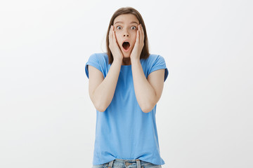 No way it cannot happen for real. Portrait of impressed and shocked funny woman in blue t-shirt, dropping jaw, shouting and staring with popped eyes at camera, holding hands on face, stunned