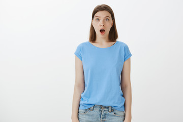 Omg, no way it is real. Shocked impressed funny girl in blue t-shirt, dropping jaw and staring at camera with interest, being stunned and amazed with friend skill, standing speechless over grey wall