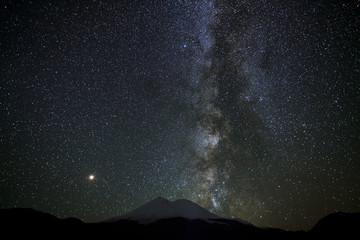 Stars of the Milky Way at night in the sky above Mount Elbrus. View of the northern slope of the two peaks of the stratovolcano. The highest peak of Russia and Europe is 5642m. 