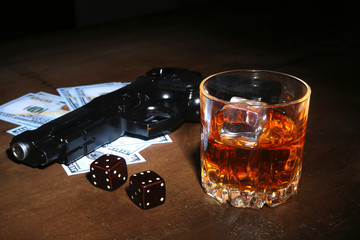 Glass of whiskey or cognac, gun, playing cards with money on the black mirror table. The concept of criminal.