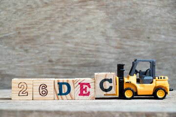 Toy forklift hold block c to complete word 26dec on wood background (Concept for calendar date 26 in month December)