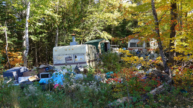 Autumn sun shines through tree canopies down on garbage and abandoned caravans