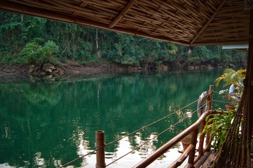 Fototapeta premium view of long-tail boat and raft house with many tourist playing in Kwai Noi River and Say Yok Yai Waterfall with green forest background, Kanchanaburi, west Thailand