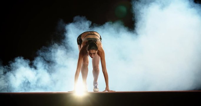 Runner speeding up. Asian female athlete blasting off in smoke on short track of stadium, training for competition