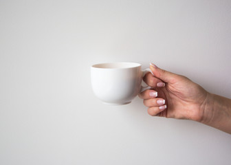 Female Hand Holding Cup of Coffee on White Wall Background