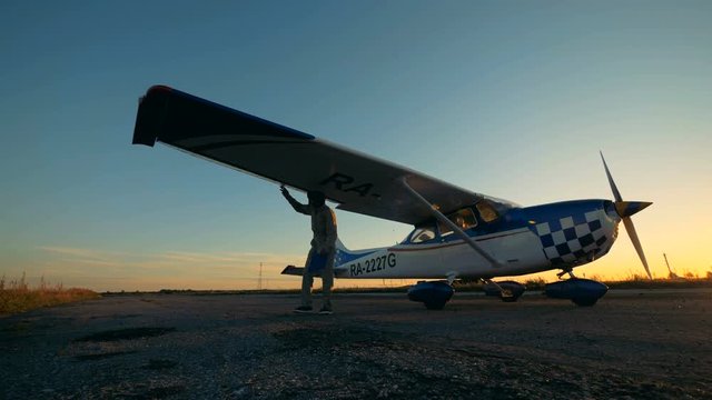 Wing of an airplane is getting inspected by a male aviator on a sunset background