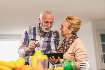 Senior couple using digital tablet and credit card in the kitchen at home for online shopping