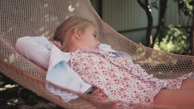 Cute child girl lying on hammock and relax at the garden.