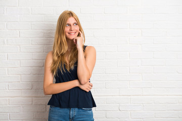 Blonde woman standing and thinking an idea on white brick wall background