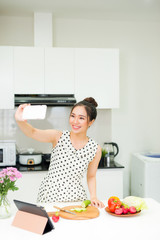 Young pretty woman using smart phone while cooking in kitchen