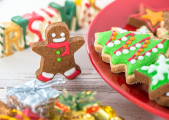 Fototapeta na wymiar Tasty and cute baked Christmas cookies (gingerbread) with beautiful xmas decoration in red plate on light wooden table background, close up, copy space (text space)