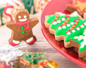 Tasty and cute baked Christmas cookies (gingerbread) with beautiful xmas decoration in red plate on light wooden table background, close up, copy space (text space)