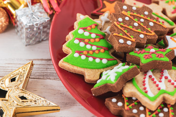 Tasty and cute baked Christmas cookies (gingerbread) with beautiful xmas decoration in red plate on light wooden table background, close up, copy space (text space)
