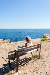 femme assise sur un banc face à la mer, falaises de Carro, Martigues, France 