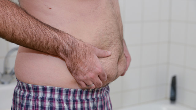 &Uuml;bergewichtiger Mann steht im Bad und kontrolliert sein Bauchfett