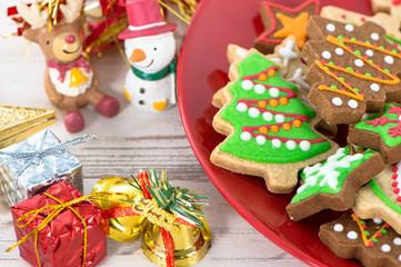 Tasty and cute baked Christmas cookies (gingerbread) with beautiful xmas decoration in red plate on light wooden table background, close up, copy space (text space)