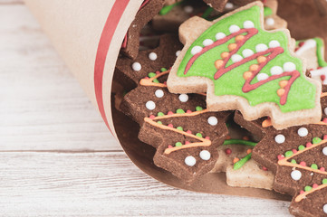 Tasty and cute baked Christmas cookies (gingerbread) with beautiful xmas decoration in paper bag on light wooden table background, close up, copy space (text space)