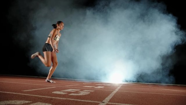 Runner heading forward. Young female athlete blasting off in smoke on short track of stadium, training before competition