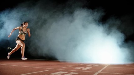 Runner heading forward. Young female athlete blasting off in smoke on short track of stadium, training before competition