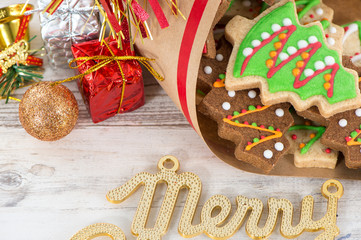 Tasty and cute baked Christmas cookies (gingerbread) with beautiful xmas decoration in paper bag on light wooden table background, close up, copy space (text space)