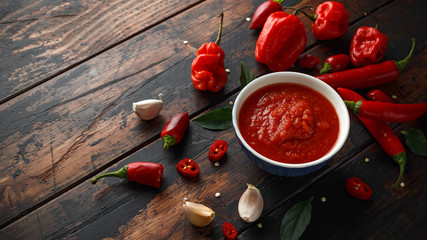 spicy hot sweet chili sauce with mix of chilli pepper, garlic and tomatoes on rustic wooden background