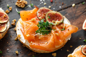 Salmon Bagel Sandwich with figs, cress salad, walnuts, cream cheese and grain on rustic wooden background. healthy breakfast