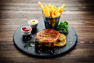 Grilled steaks with french fries served on black stone on wooden table