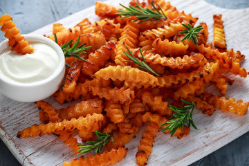 Baked butternut squash fries with sea salt and rosemary. Pumpkin chips on white wooden board.