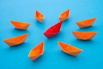 Leadership concept. Red paper boat origami motivate meeting with small orange boat on blue...