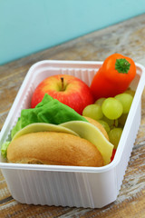 Lunchbox containing cheese roll with lettuce and tomato, crunchy pepper, red apple and grapes
