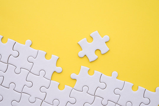 Unfinished white jigsaw puzzle on yellow background. Business strategy teamwork and problem solving concept. Teamwork is collaborative effort of team to achieve goal or to complete task.