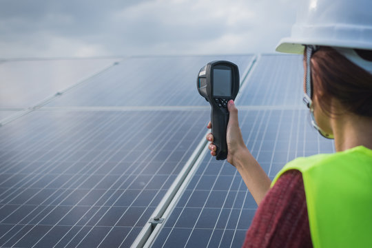 woman engineer checking heat of solar panel and using ir camera to scan heating of panel at solar power plant ; infrared camera using for checking and maintenance power plant of solar