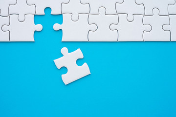 Fototapeta premium The last piece of jigsaw puzzle to complete task on blue background. Business strategy teamwork, problem solving concept. Teamwork is collaborative effort of team to achieve goal or complete mission.