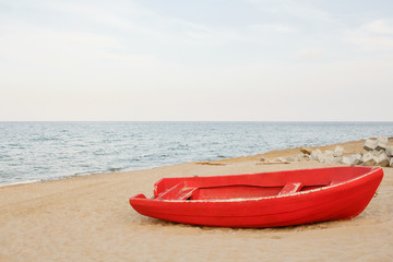 Old red boat on the beach, waves on the water and sky background