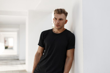 Handsome young american stylish man with hairstyle in fashion black shirt standing near white wall