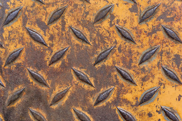 Close-up of old weathered rusty brown industrial anti slip metal plate with diamond pattern and worn yellow paint   